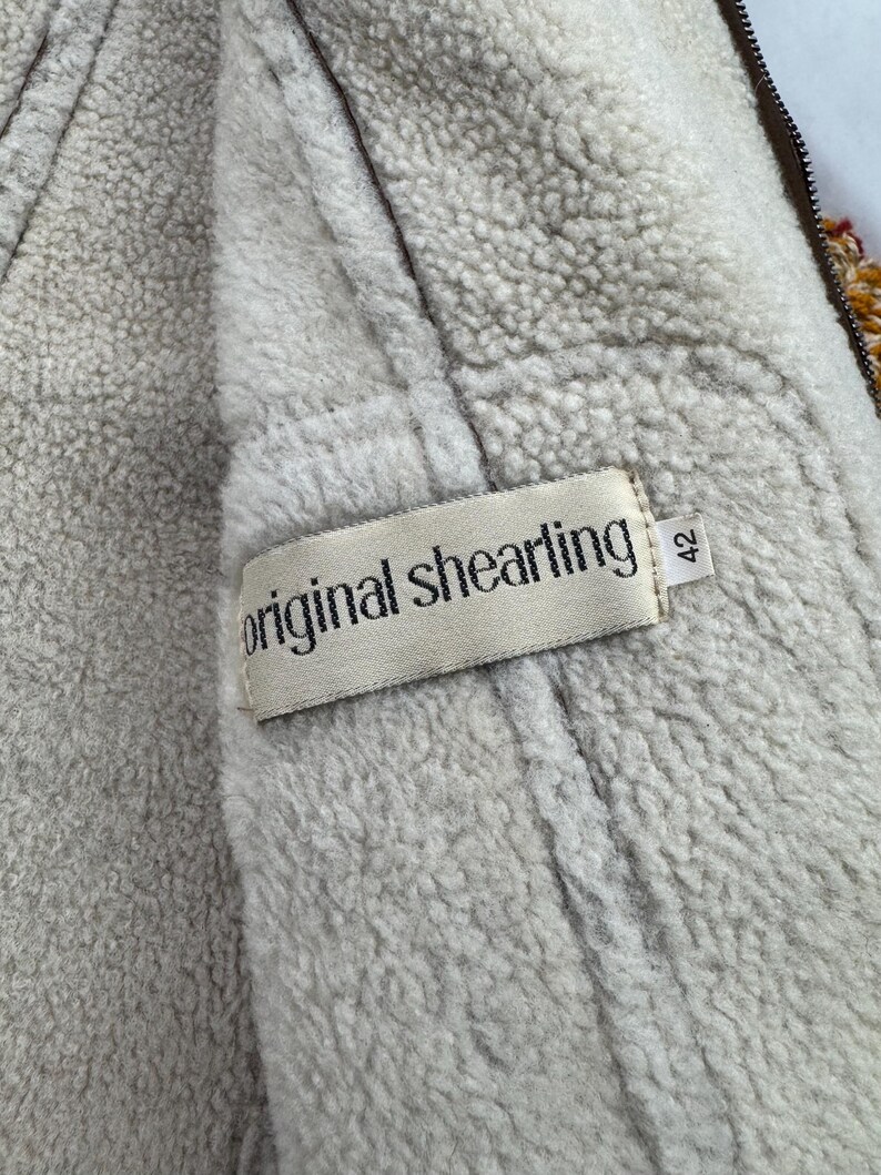 May include: Close-up of a vintage shearling jacket interior. The jacket features a cream-colored, fluffy lining and a brown exterior. A tag reads "original shearling" with the size "42".
