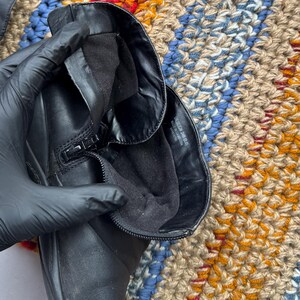 May include: Black leather boot with a zipper closure. The boot's interior is lined with black fabric. The boot is shown against a colorful, textured background. The boot appears to be in good condition.