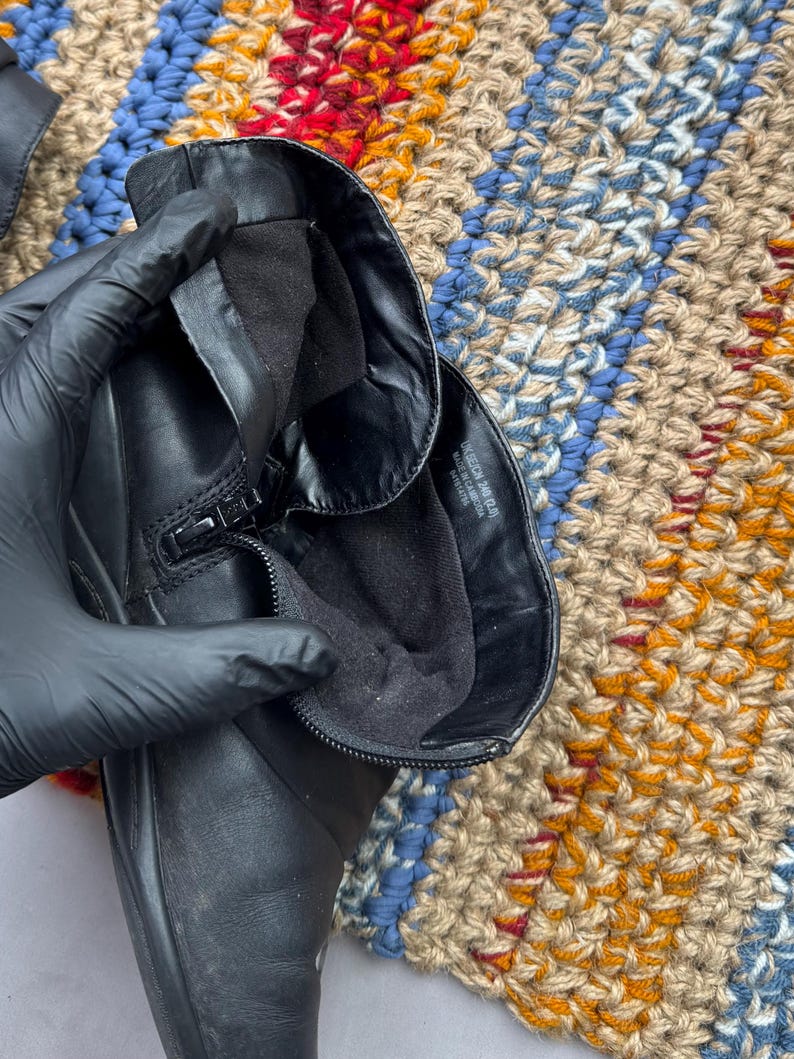 May include: Black leather boot with a zipper closure. The boot's interior is lined with black fabric. The boot is shown against a colorful, textured background. The boot appears to be in good condition.