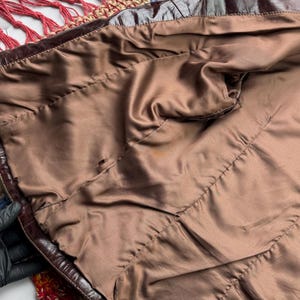 Pu&ograve; includere: L'interno di una giacca di pelle marrone con una fodera in raso marrone. La giacca &egrave; appoggiata su una coperta all'uncinetto colorata.
