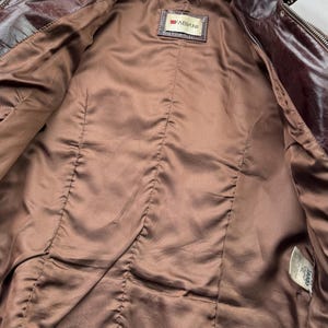 Pu&ograve; includere: Giacca di pelle marrone con chiusura a zip e un'etichetta che recita "FABIANI". La giacca &egrave; non foderata e ha una fodera in raso marrone.