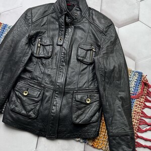 May include: A black leather jacket with multiple pockets and a zipper closure. The jacket has a stand-up collar and long sleeves.
