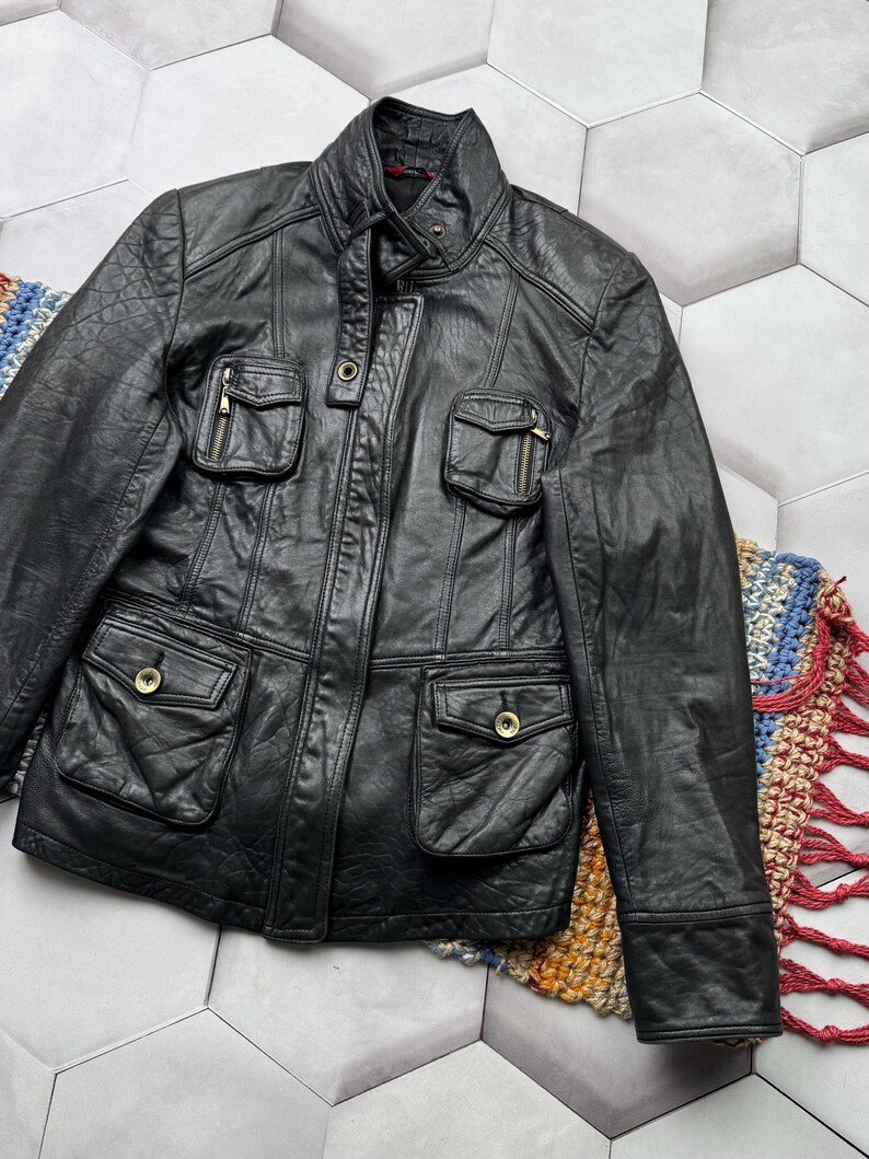 May include: A black leather jacket with multiple pockets and a zipper closure. The jacket has a stand-up collar and long sleeves.