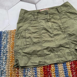 May include: A green cargo skirt with a button fastening and multiple pockets. The skirt has a drawstring at the bottom.