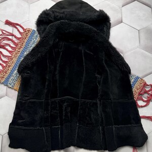 May include: A black hooded coat with a plush, textured interior and exterior. The coat features a hood and a button closure. The garment is displayed on a patterned surface.