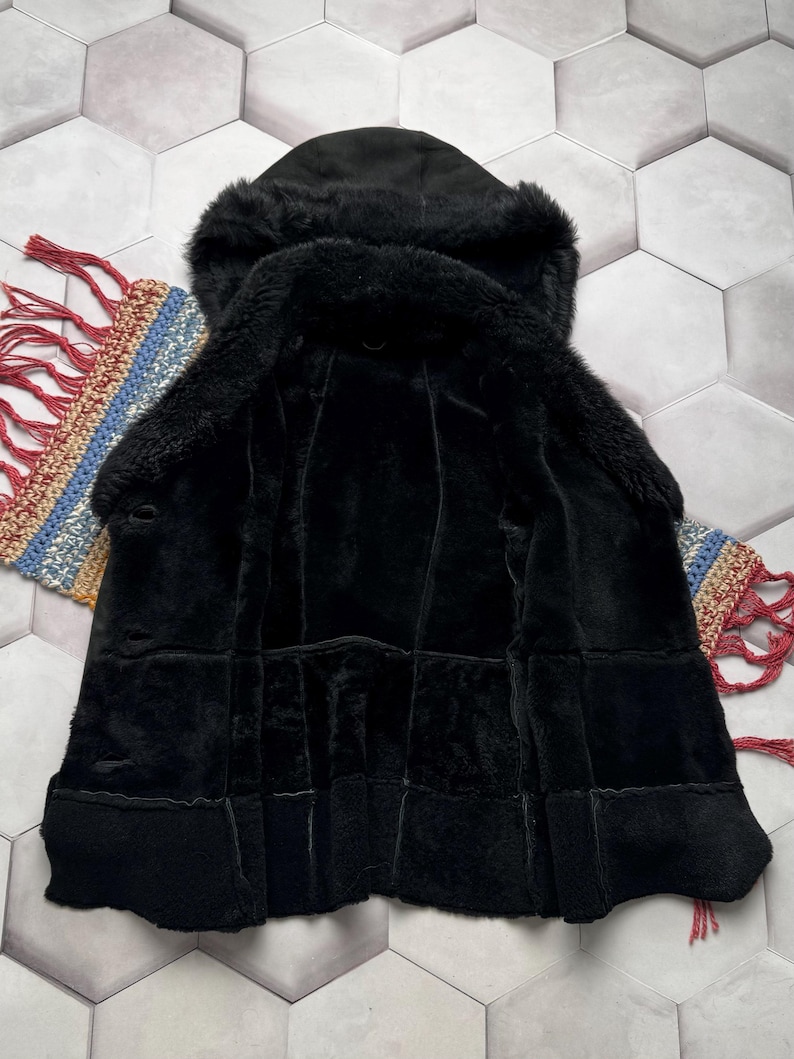 May include: A black hooded coat with a plush, textured interior and exterior. The coat features a hood and a button closure. The garment is displayed on a patterned surface.
