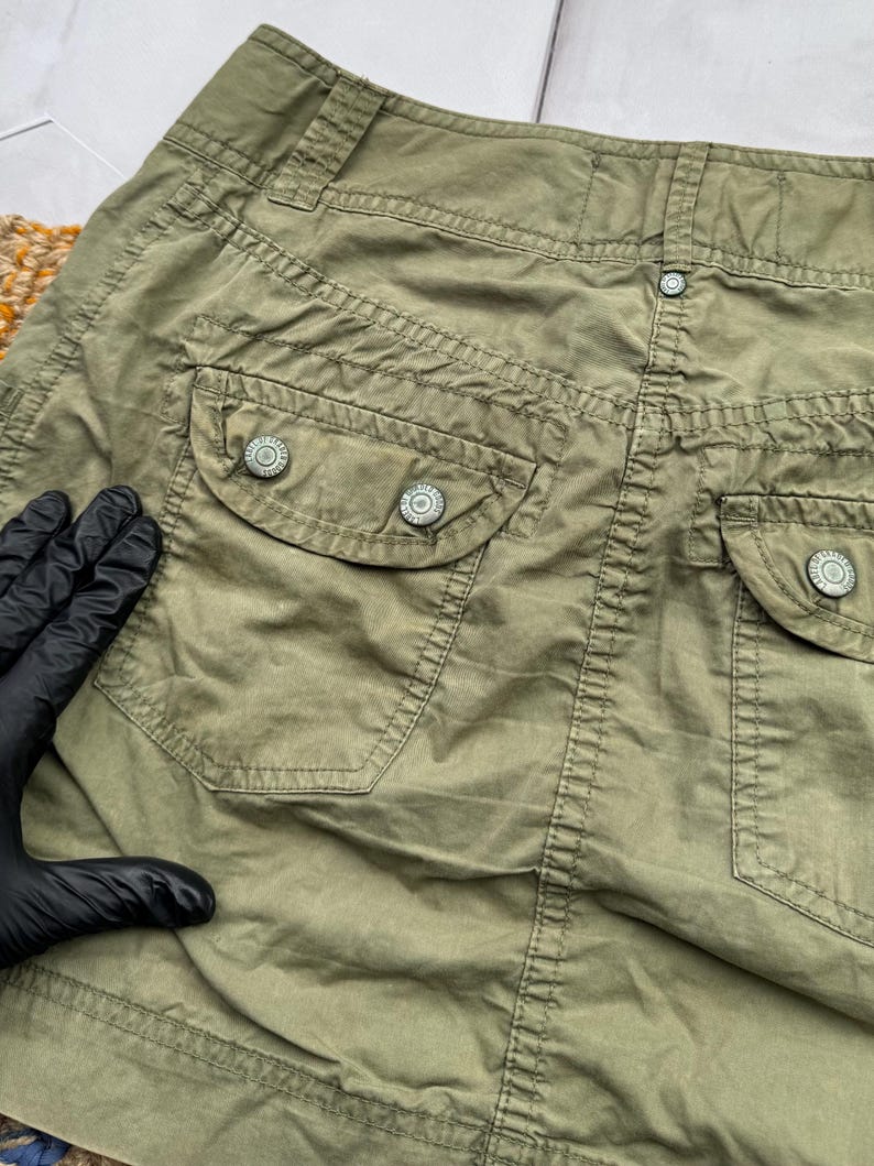 May include: A green cargo skirt with two large pockets and button closures. The skirt is made of a lightweight, durable fabric.