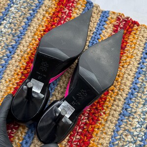 May include: A pair of black high-heeled shoes with pointed toes. The heels are about 4 inches tall and the shoes have a pink trim around the edges. The shoes are made of leather and have a size 37 label on the bottom.