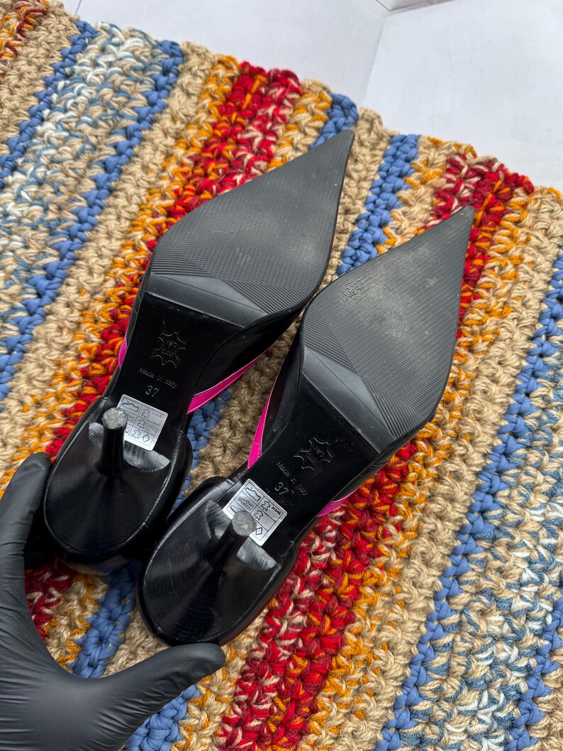 May include: A pair of black high-heeled shoes with pointed toes. The heels are about 4 inches tall and the shoes have a pink trim around the edges. The shoes are made of leather and have a size 37 label on the bottom.