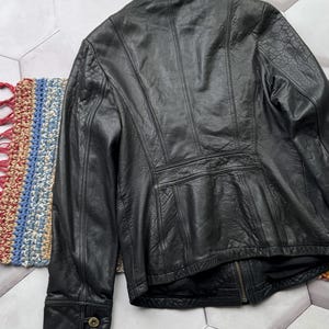 May include: A black leather jacket with a zipper closure and buttoned cuffs. The jacket has a stand-up collar and a fitted silhouette.
