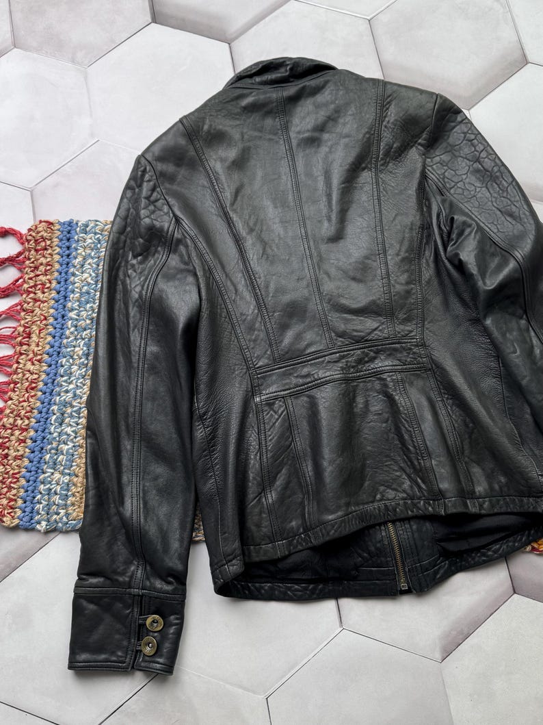 May include: A black leather jacket with a zipper closure and buttoned cuffs. The jacket has a stand-up collar and a fitted silhouette.