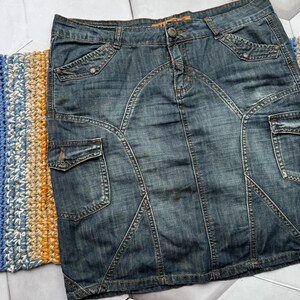 Puede incluir: Una falda vaquera con un lavado azul descolorido. La falda presenta m&uacute;ltiples bolsillos, costuras decorativas y cierre de bot&oacute;n. La falda tiene un estilo cl&aacute;sico y casual.