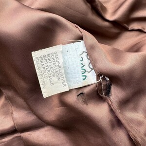 Pu&ograve; includere: Una giacca di pelle marrone con un'etichetta che recita "Genuine Leather, Echtes Leder, Echt Leder, Cuir Veritable, Vera Pelle, Piel Autentica".