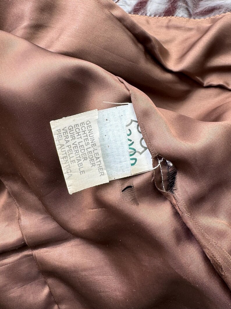 Pu&ograve; includere: Una giacca di pelle marrone con un'etichetta che recita "Genuine Leather, Echtes Leder, Echt Leder, Cuir Veritable, Vera Pelle, Piel Autentica".