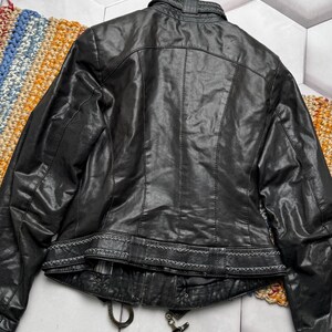 K&ouml;nnte beinhalten: Schwarze Lederjacke mit dekorativen N&auml;hten an Kragen und Taille. Die Jacke hat einen Rei&szlig;verschluss und eine strukturierte Optik. Die R&uuml;ckseite der Jacke ist sichtbar und zeigt das Design und die Nahtdetails.