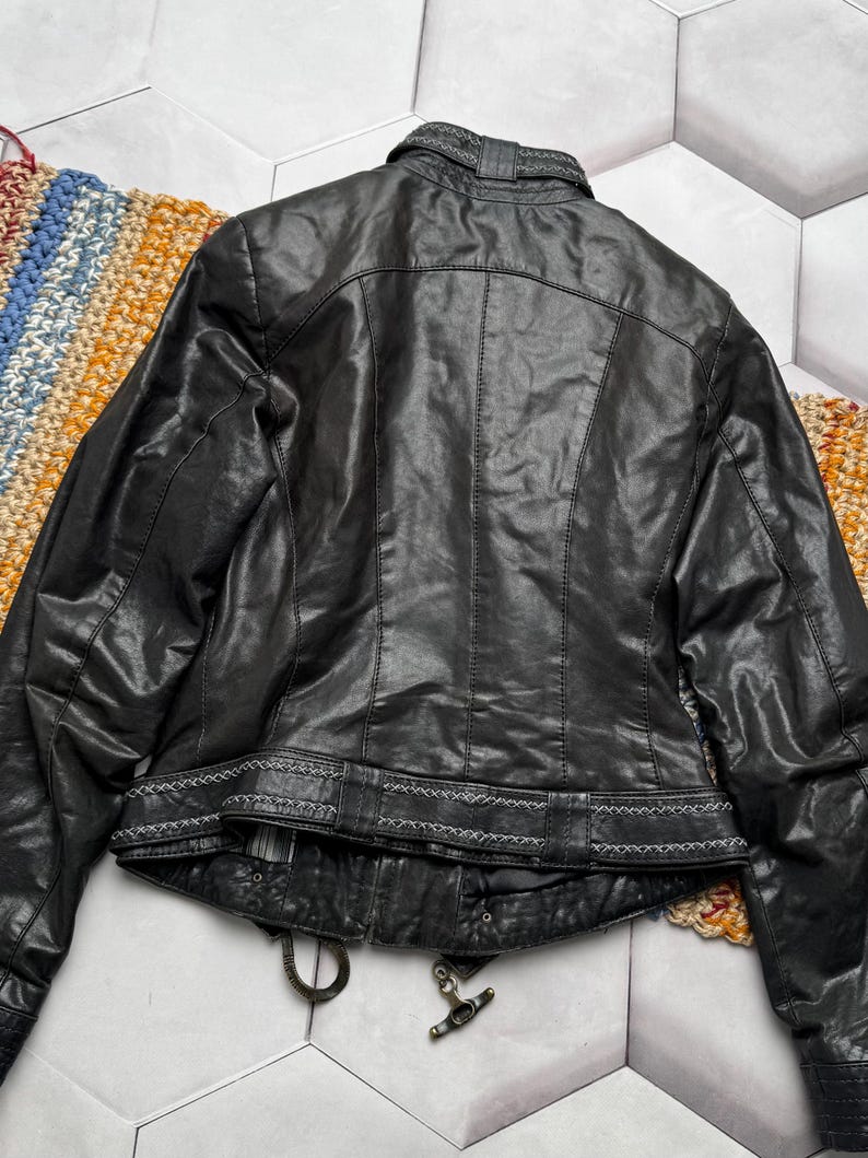 K&ouml;nnte beinhalten: Schwarze Lederjacke mit dekorativen N&auml;hten an Kragen und Taille. Die Jacke hat einen Rei&szlig;verschluss und eine strukturierte Optik. Die R&uuml;ckseite der Jacke ist sichtbar und zeigt das Design und die Nahtdetails.