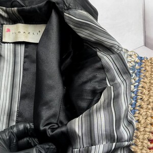 K&ouml;nnte beinhalten: Nahaufnahme einer schwarzen Lederjacke mit gestreiftem Innenfutter. Das Jackeninnere besteht aus einem schwarzen, satinartigen Material und tr&auml;gt das Etikett "ILGAZLI". Das Futter hat d&uuml;nne, vertikale grau-wei&szlig;e Streifen.