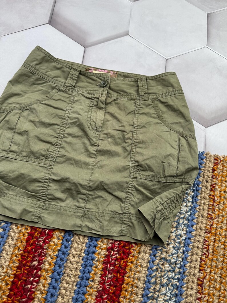 May include: A green cargo skirt with multiple pockets and a button fastening. The skirt is made from a lightweight fabric and has a relaxed fit.