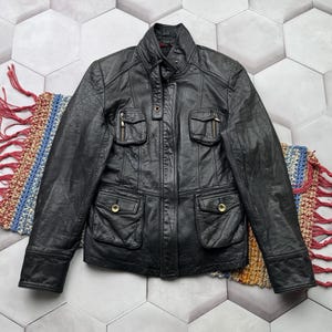 May include: A black leather jacket with a stand-up collar, zipper closure, and multiple pockets. The jacket has a slightly distressed look.