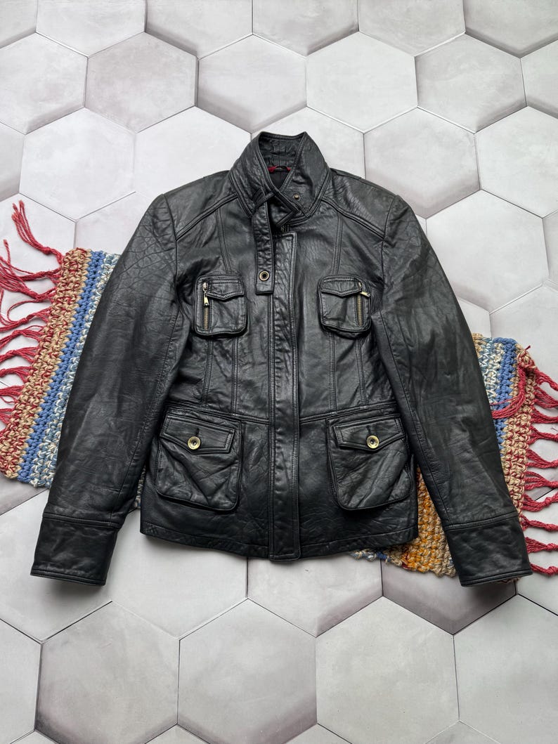 May include: A black leather jacket with a stand-up collar, zipper closure, and multiple pockets. The jacket has a slightly distressed look.