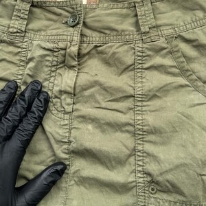 May include: A green cargo skirt with a button fastening and a pocket on the right side. The skirt is made from a lightweight, cotton fabric.