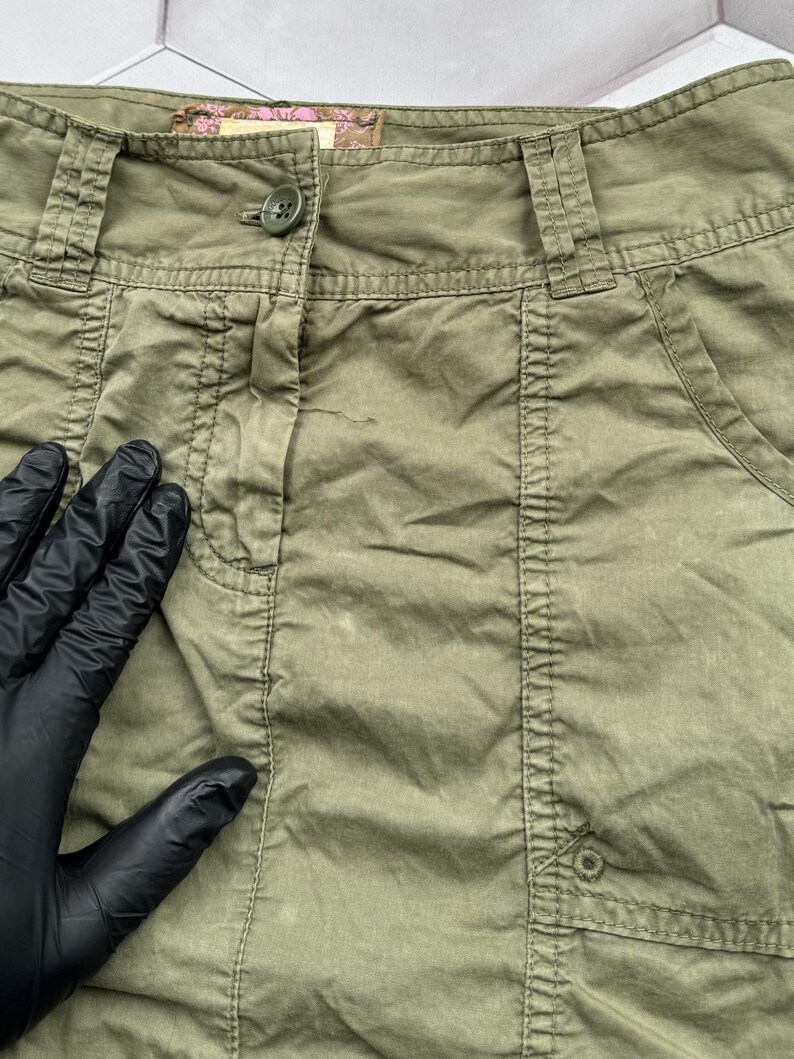 May include: A green cargo skirt with a button fastening and a pocket on the right side. The skirt is made from a lightweight, cotton fabric.