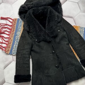 May include: A black coat with a hood and faux fur trim. The coat has a button closure and fur trim on the cuffs. The coat is made of a suede-like material. The coat is displayed on a patterned surface.