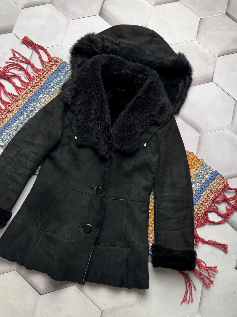 May include: Black hooded coat with a faux fur collar and trim. The coat features a button-up front and a tailored fit. The hood is also trimmed with faux fur. The coat is made of a soft, suede-like material.