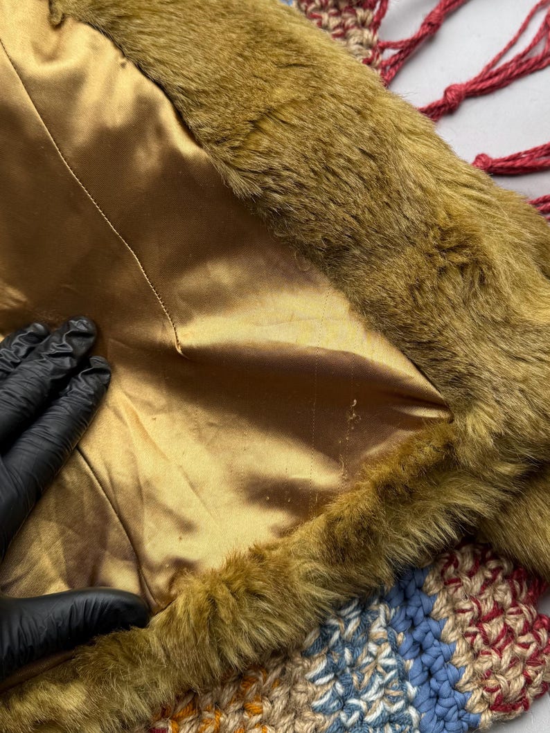 May include: Close-up of a brown faux fur trim with a gold satin lining. The fur is soft and fluffy, and the lining is smooth and silky.