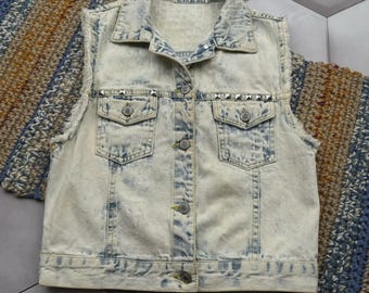 May include: A light-wash denim vest with a button-up front, two chest pockets, and silver stud accents. The vest has a distressed look with frayed edges and a classic collar. The vest is sleeveless.