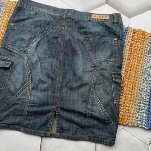 Puede incluir: Falda vaquera de color azul medio, de largo hasta la rodilla. Presenta bolsillos cargo, costuras decorativas y una peque&ntilde;a abertura en la parte trasera. La etiqueta de la marca "N-UNO" es visible en la cintura.