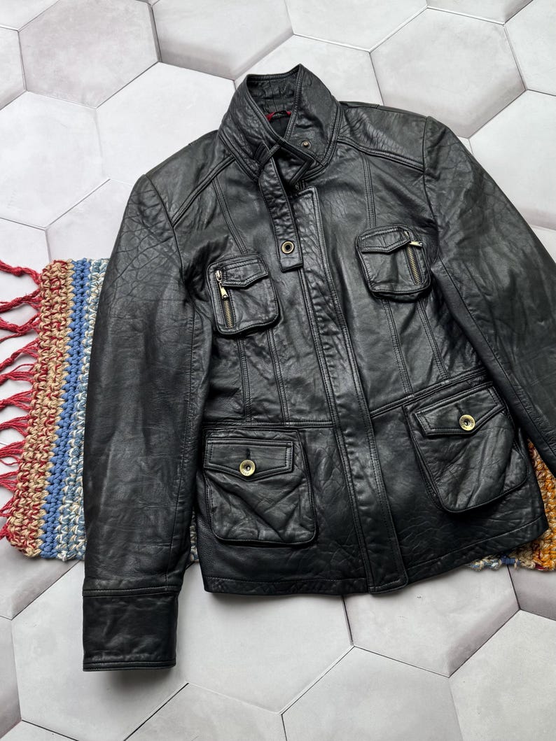 May include: A black leather jacket with a zipper closure and multiple pockets. The jacket has a stand-up collar and a quilted lining.