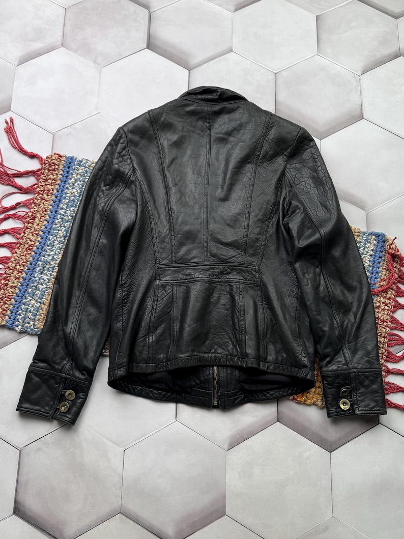 May include: A black leather jacket with a zipper closure and button accents on the cuffs. The jacket has a fitted silhouette and a stand-up collar.