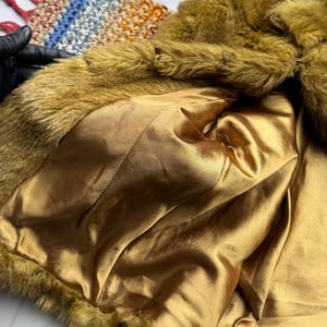 May include: A mustard yellow faux fur jacket with a gold satin lining. The jacket is unbuttoned and the lining is visible.