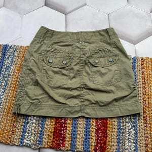 May include: A green cargo skirt with two large pockets on the back. The skirt is made of a thick, durable fabric.