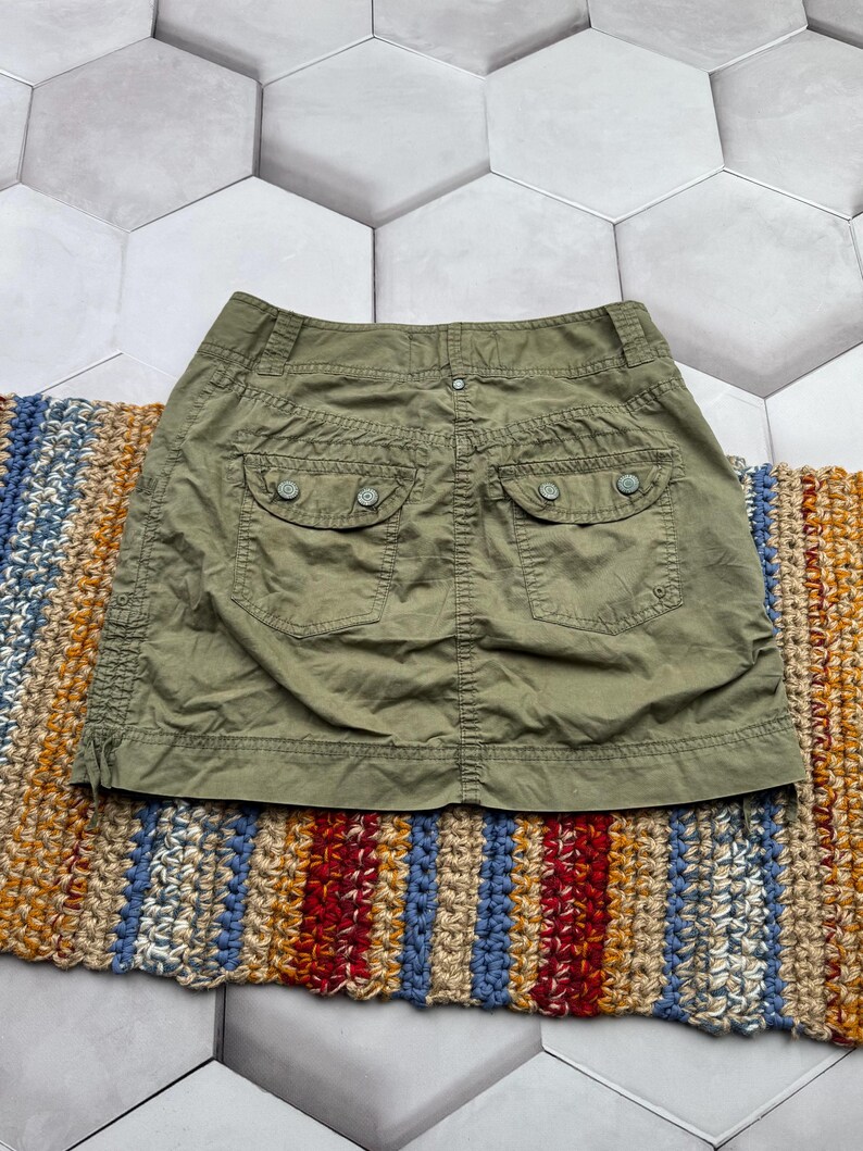 May include: A green cargo skirt with two large pockets on the back. The skirt is made of a thick, durable fabric.