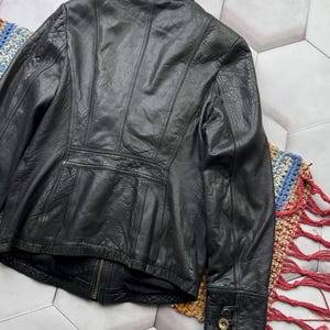May include: Black leather jacket with a zipper closure and buttoned cuffs. The jacket has a textured surface and a fitted silhouette.