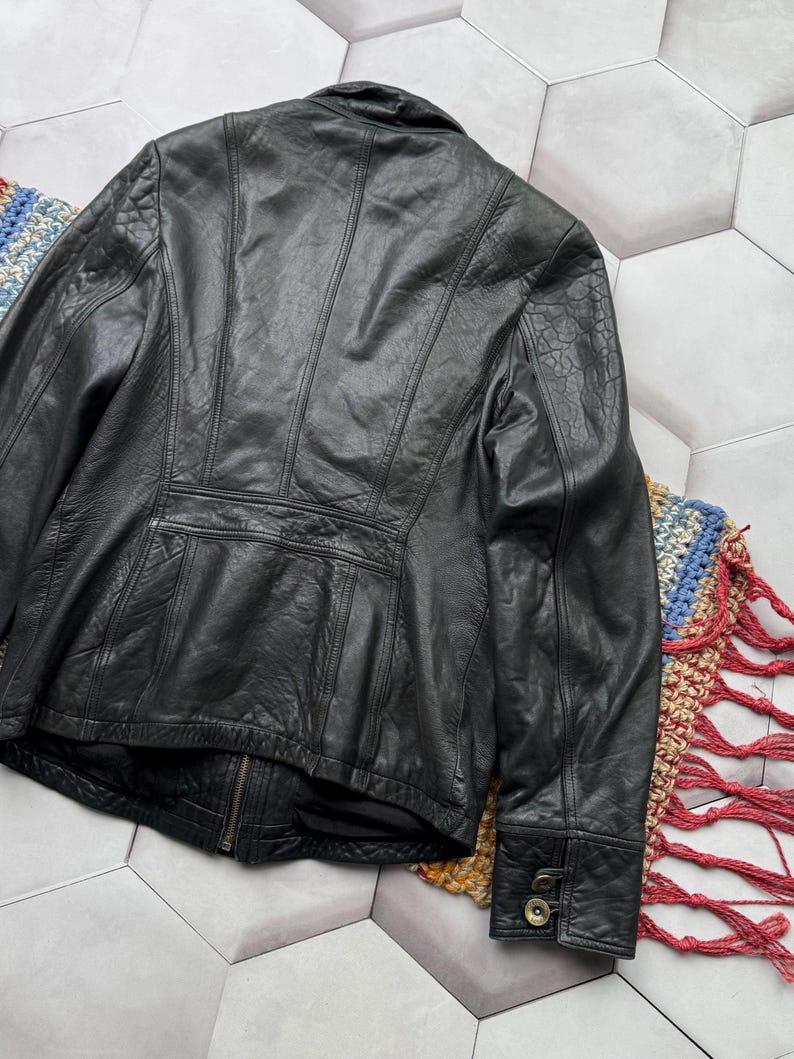 May include: Black leather jacket with a zipper closure and buttoned cuffs. The jacket has a textured surface and a fitted silhouette.