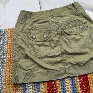 May include: A green cargo skirt with two large pockets on the back. The skirt has a button closure and a zip fly.