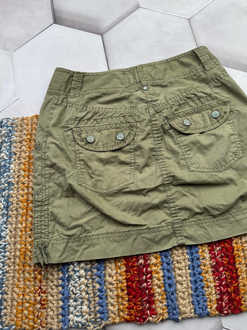 May include: A green cargo skirt with two large pockets on the back. The skirt has a button closure and a zip fly.