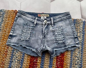 May include: Light blue denim shorts with distressed details and rhinestones. The shorts have a frayed hem and a  "Yumi Kim" brand label.
