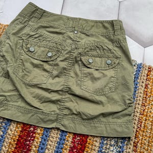 May include: A green cargo skirt with two back pockets and a button fastening. The skirt is made from a lightweight fabric and has a relaxed fit.