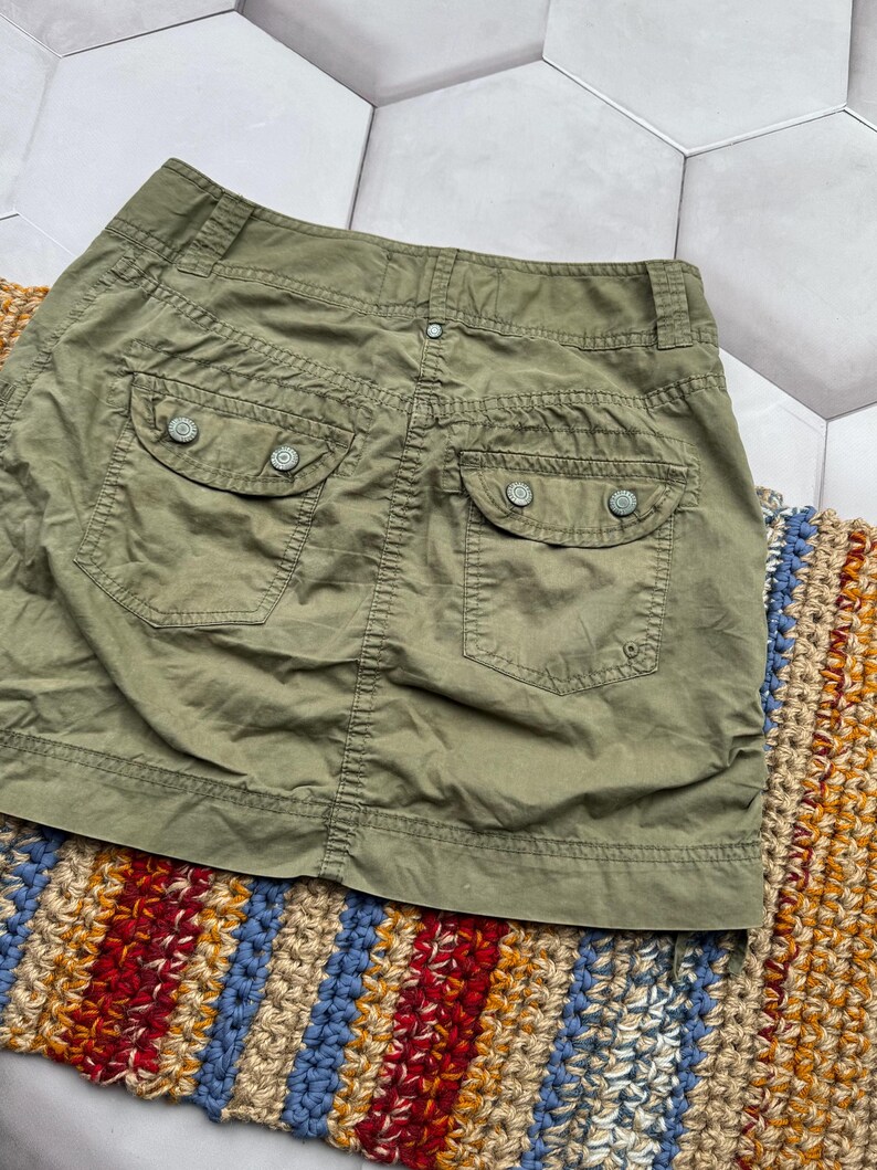 May include: A green cargo skirt with two back pockets and a button fastening. The skirt is made from a lightweight fabric and has a relaxed fit.