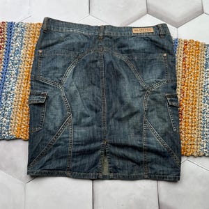Puede incluir: Falda vaquera azul descolorido. Cuenta con bolsillos cargo, costuras decorativas y una abertura trasera. La etiqueta "N-UNO" es visible en la cintura. La falda es de estilo hasta la rodilla.