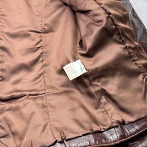 Pu&ograve; includere: L'interno di una giacca di pelle marrone con fodera marrone. Un'etichetta bianca con la scritta "Made in Italy" &egrave; visibile.