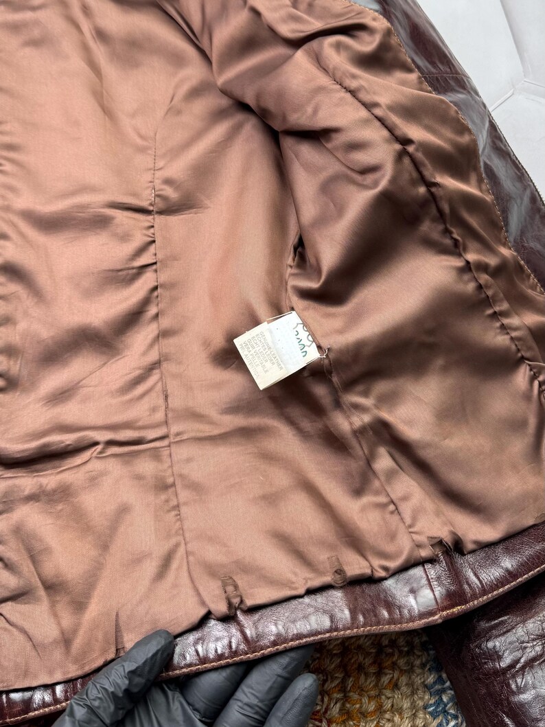 Pu&ograve; includere: L'interno di una giacca di pelle marrone con fodera marrone. Un'etichetta bianca con la scritta "Made in Italy" &egrave; visibile.