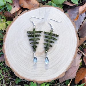 以下が含まれることがあります： 緑色のシダの形をしたイヤリングのペア。涙の形をした青い宝石のアクセントが施されています。