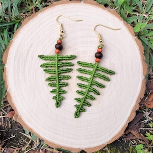 Könnte beinhalten: Ein Paar grüne Ohrringe in Form von Farnen mit braunen und orangefarbenen Holzperlen und goldenen Haken.