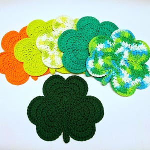 May include: A collection of handmade crochet shamrock coasters in various colors, including orange, green, yellow, and blue. The coasters are arranged on a white surface, showcasing their detailed stitch work and vibrant hues. These decorative items are perfect for St. Patrick's Day.