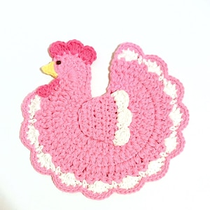 May include: A pink crocheted chicken dishcloth with white trim. The chicken has a yellow beak and a pink comb.